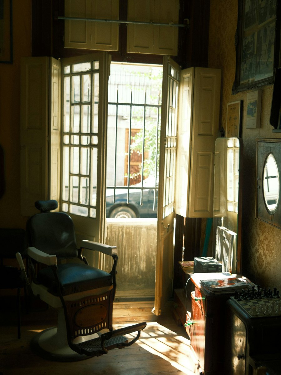 A barber's chair beside a shop door standing open onto a sunlit street