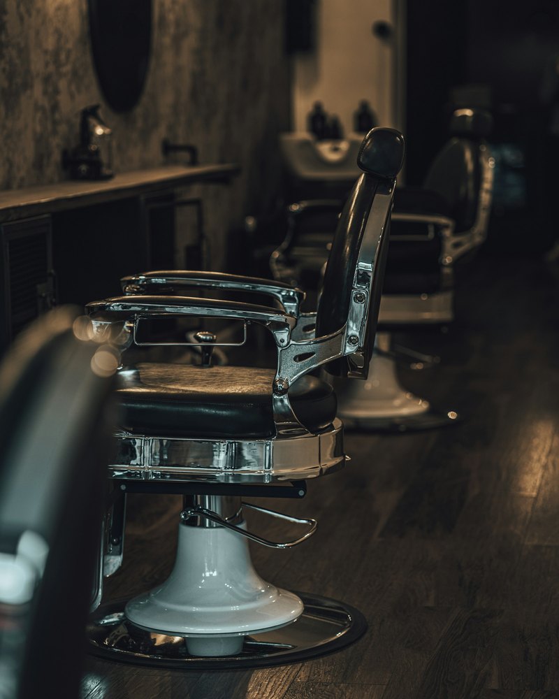 A barber chair in profile with a second chair and the counter behind it